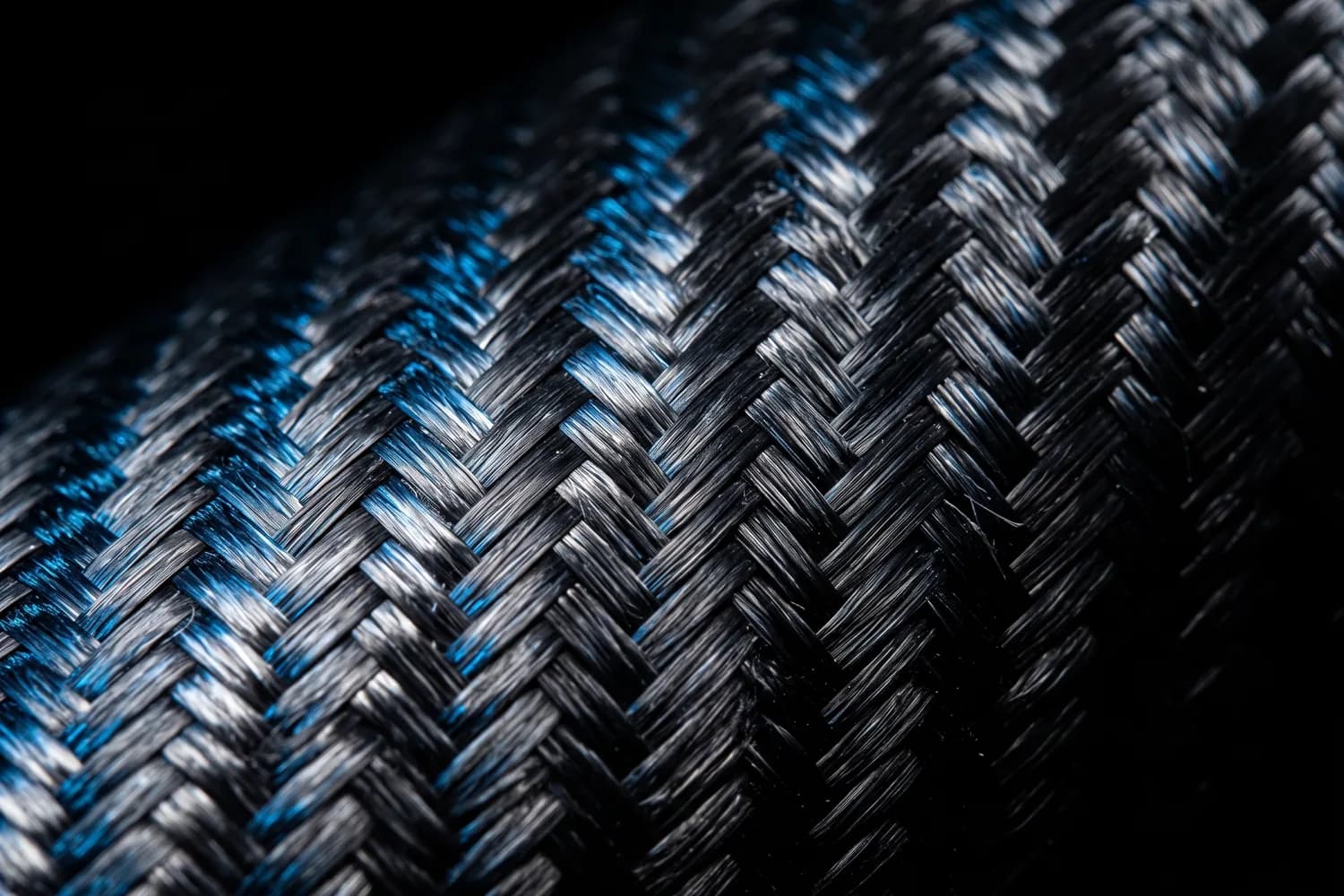 Gros plan sur un tissage serré de fibre de carbone noire parcouru de fils bleus, sous une lumière rasante sur fond noir