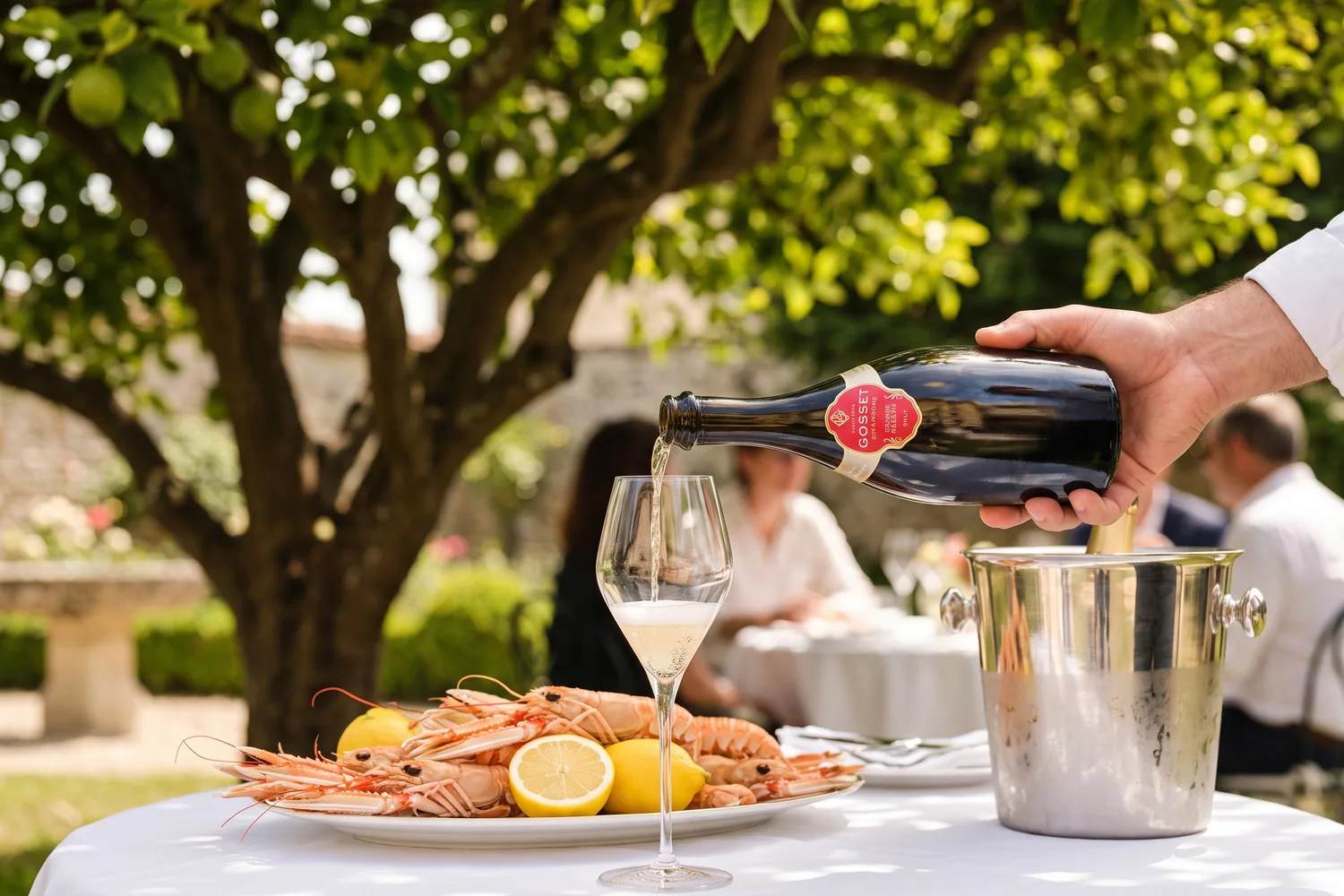 A bottle of Gosset Grande Réserve served in an antique bottle at a summer lunch in a garden in Aÿ, accompanied by an ice bucket and a platter of langoustines
